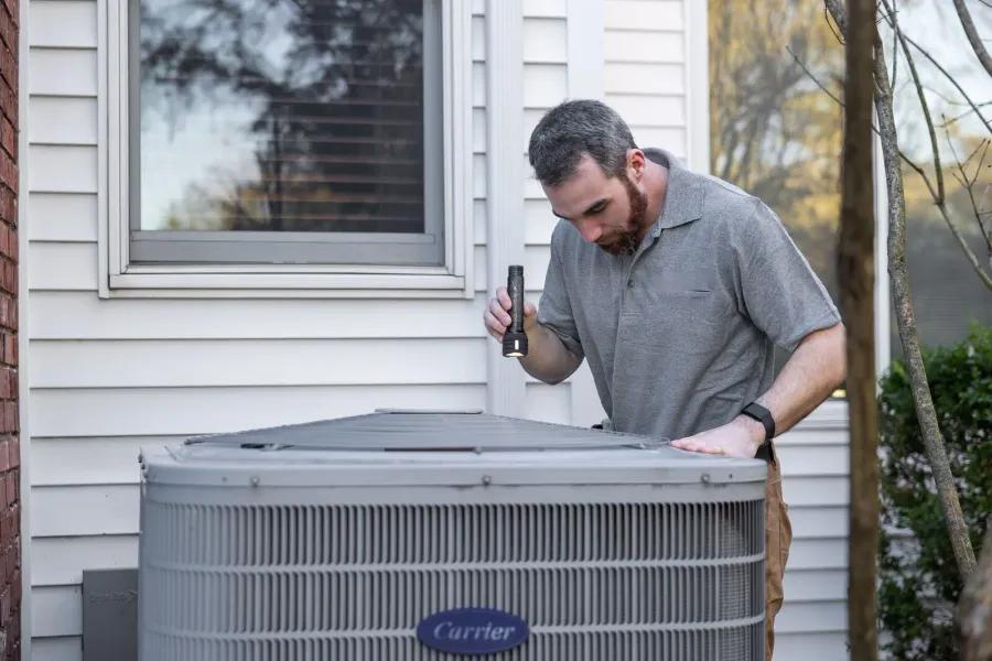 A technician performing routine AC maintenance and inspecting outdoor equipment